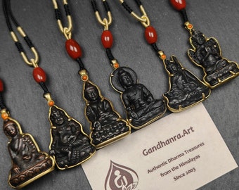 May include: Seven black metal pendants with gold accents, each featuring a different deity or figure, hanging from black cords with red beads. The pendants are displayed on a white card with the text "Gandhanra.Art Authentic Dharma Treasures from the Himalayas Since 2003".