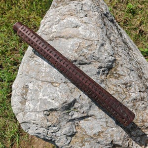 May include: A dark brown wooden stick with intricate carvings covering its entire surface. The stick is lying on a gray rock.