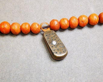 May include: A brown wooden bead necklace with a metal charm attached. The charm is a small, rectangular box with a patterned design.