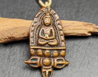 May include: Bronze-colored pendant necklace featuring a seated Buddha figure. The pendant has an arched top and a detailed design, including a lotus base and a stylized emblem at the bottom. The necklace has a woven cord.