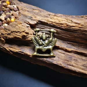May include: A small, gold-colored metal pendant depicting a mythical creature with wings and a crown. The pendant is on a wooden surface.