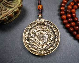 Puede incluir: Un collar con un colgante redondo dorado, con un diseño central de flor de loto rodeado de doce animales del zodíaco. El colgante está unido a un cordón marrón con una pequeña cuenta marrón.