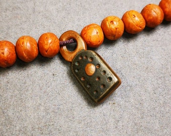 May include: A brown wooden beaded necklace with a metal clasp. The clasp has a circular design with a small, round, copper-colored accent.