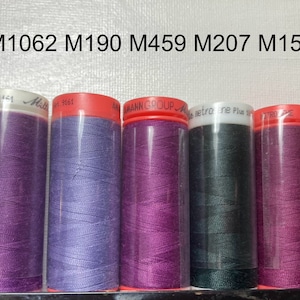 May include: Five spools of thread in different colours: purple, lavender, pink, dark green, and burgundy. The spools are labelled with the numbers M1062, M190, M459, M207, and M157.