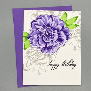 May include: A white card with a purple flower and green leaves. The card has the text "happy birthday" written on it.
