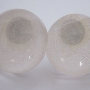 May include: Two white glass eyes with a textured surface. The eyes are round and have a slight shimmer.