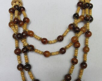 May include: A multi-strand necklace made of brown and beige wooden beads. The necklace has a layered look with three strands of beads.