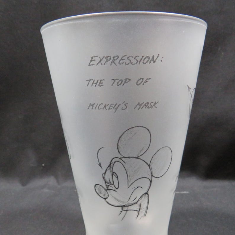 Op de afbeelding: Matte glazen beker met een schets van Mickey Mouse. De beker heeft de tekst "EXPRESSION: THE TOP OF MICKEY'S MASK" in een handschrift. Het ontwerp bevat een schets van Mickey's gezicht.