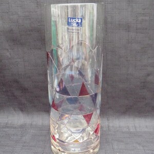 May include: A clear glass vase with a geometric pattern of red, white, and blue. The vase has a label that reads "Lucka Glas Mundgeblasen Handgefertigt".