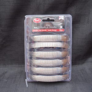May include: A package of six satin nickel dimple pull handles. The handles are 96mm long and are labeled "Elite Knobs & Handles" by the brand "Hiatt". The handles have a series of small dimples across the surface.