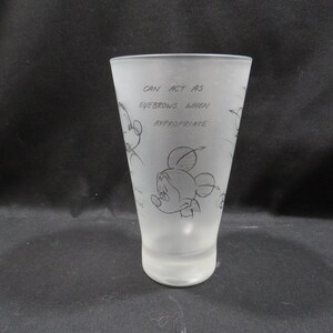 Op de afbeelding: Matte glazen tumbler met schetsen van Mickey Mouse en de tekst "CAN ACT AS EYEBROWS WHEN APPROPRIATE." De cilindervormige beker is geschikt voor drankjes. Het ontwerp is een speelse verwijzing naar het beroemde stripfiguur.