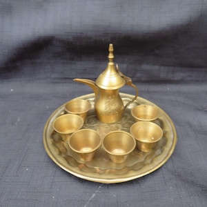 May include: A vintage brass coffee set, including a decorative coffee pot with a long spout, a tray, and six small cups. The set has an ornate design and a warm, golden color.