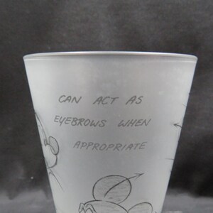 Op de afbeelding: Een matglas met een cartoontekening van Mickey Mouse. De tekst op het glas luidt "CAN ACT AS EYEBROWS WHEN APPROPRIATE". Het glas heeft een licht taps toelopende vorm.