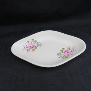 May include: White, diamond-shaped ceramic dish with pink rose floral pattern. The dish has a slightly raised edge and is decorated with pink roses, blue forget-me-nots, and yellow accents. A vintage-style serving piece.