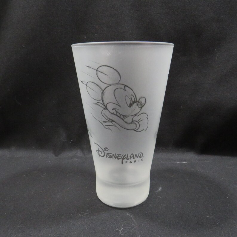 Op de afbeelding: Matte glazen tumbler met een schets van Mickey Mouse in beweging. De woorden "Disneyland Paris" staan op het glas. De tumbler is cilindrisch met een licht uitlopende bovenkant.