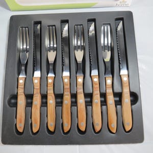 May include: A set of eight stainless steel steak knives and forks with wooden handles, arranged in a black tray. The knives have serrated blades, and the forks have three tines. The handles are light brown with a silver rivet.