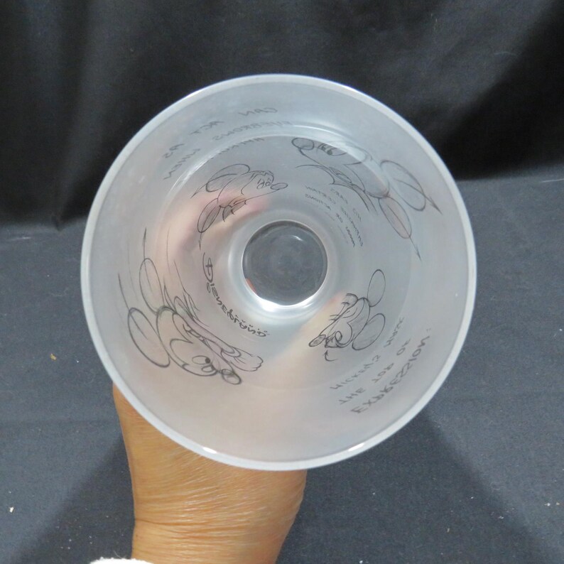 Op de afbeelding: Een helder, mat glas met zwarte lijntekeningen van Mickey Mouse en tekst. Het glas heeft een brede opening en loopt taps toe naar een kleinere basis. De tekst bevat de woorden "Expression" en "The Art of".