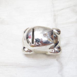 Puede incluir: Una alcancía de coche de plata con una ranura en la parte superior para monedas.