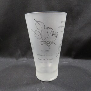 Op de afbeelding: Een mat glas met een schets van Mickey Mouse. De illustratie bevat Mickey's oren en de tekst "HIS EARS EMPHASIZE CERTAIN MOODS OR ACTIONS". Het glas is taps toelopend en heeft een gladde, matte afwerking.