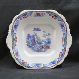 May include: White square serving dish with a scalloped edge and two handles. The dish features a colorful Asian-inspired landscape scene in the center, with a pagoda, bridge, and water. The rim has a blue, red, and gold decorative border.