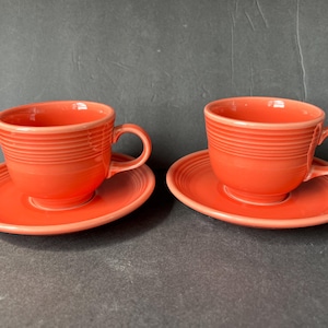 Puede incluir: Dos tazas de té y platillos de cerámica de color coral. Las tazas tienen un diseño acanalado y están colocadas sobre platillos a juego.