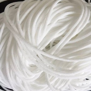 May include: A close-up of a large spool of white elastic cord. The cord is tightly wound and appears to be soft and flexible.