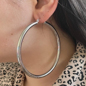 May include: A large, shiny silver hoop earring. The earring is round and has a smooth, reflective surface. The earring is worn in the ear. The background includes a leopard print pattern.