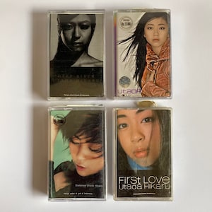 May include: Four cassette tapes featuring the Japanese singer Utada Hikaru. The tapes are in clear plastic cases with colorful artwork. The titles of the tapes are "Deep River", "Distance", "First Love", and "Utada Exclus".