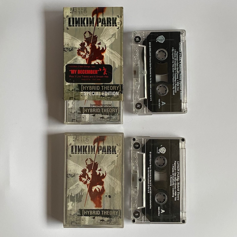 以下が含まれることがあります： リンキン・パークのアルバム「ハイブリッド・セオリー」の2つのカセットテープ。アルバムカバーには、鎌を持った人物の赤と黒のシルエットが描かれている。カセットテープケースには「ハイブリッド・セオリー」という文字が印刷されている。
