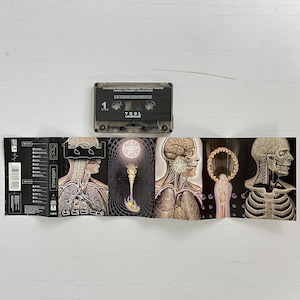 May include: A cassette tape of Tool's album "Lateralus" with a black and white image of a human body on the front. The cassette tape is in a clear plastic case with a black label. The album title is printed in white on the label.