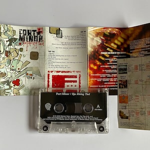 以下が含まれることがあります： 透明なカセットテープケースで、黒いラベルには「Fort Minor / The Rising Tied」と書いてあります。ラベルにはワーナー・ブラザース・レコードのロゴとアルバムの著作権情報も含まれています。