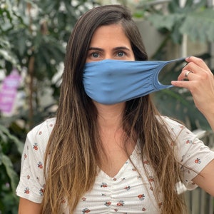 Puede incluir: Una mujer con una mascarilla facial azul claro y una camisa de estampado floral blanco.