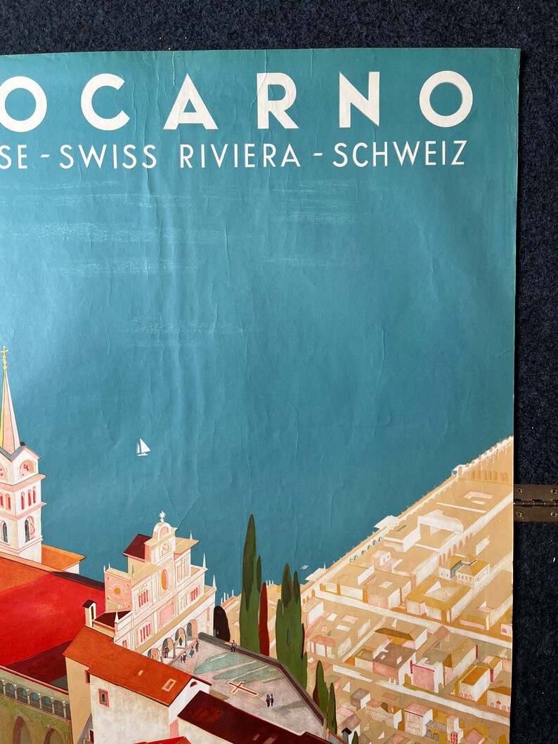 May include: A vintage travel poster advertising the Swiss Riviera town of Locarno. The poster features a colorful illustration of the town with a church, buildings, and trees. The text "Locarno" is in large white letters at the top of the poster, and the text "SE - SWISS RIVIERA - SCHWEIZ" is in smaller white letters below it.
