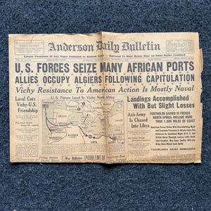 Puede incluir: Un recorte de periódico en blanco y negro del Anderson Daily Bulletin fechado el 10 de noviembre de 1942, con el titular "U.S. FORCES SEIZE MANY AFRICAN PORTS". El artículo trata sobre la ocupación aliada de Argel y el desembarco de las fuerzas estadounidenses en el norte de África de Vichy. Se incluye un mapa del norte de África que muestra las ubicaciones de los desembarcos.