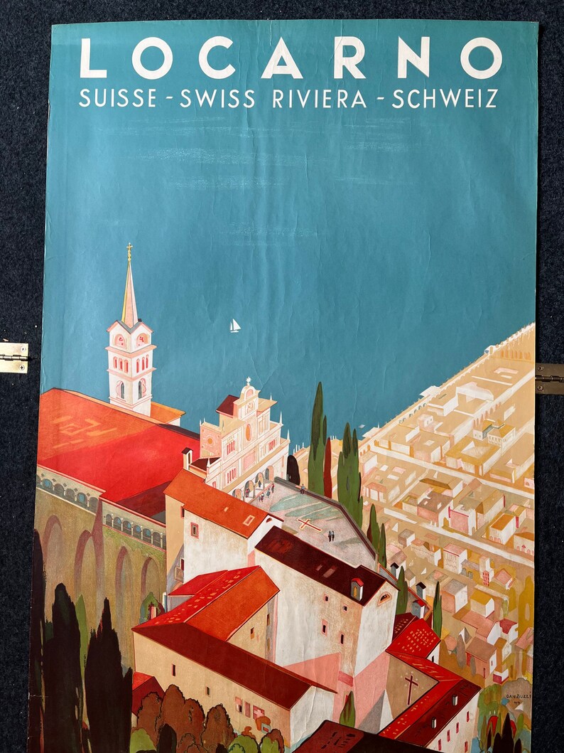 May include: A vintage travel poster advertising the Swiss Riviera town of Locarno. The poster features a colorful illustration of the town's architecture, including a church with a tall steeple, and a view of the lake. The text "Locarno" is written in large, bold letters at the top of the poster, and the text "Suisse - Swiss Riviera - Schweiz" is written below it.
