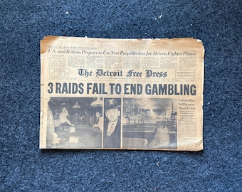 May include: A vintage newspaper headline from The Detroit Free Press dated January 7, 1948, reads "3 Raids Fail to End Gambling". The headline is in bold, large font. The newspaper is yellowed with age and has a photo of a man in a suit and hat.