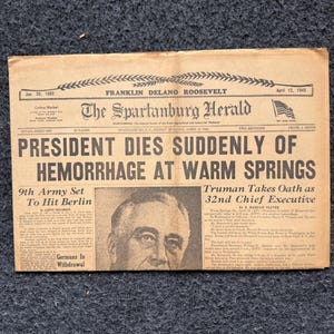 May include: An aged, tan-coloured newspaper titled The Spartanburg Herald, dated April 13, 1945. The headline reads President Dies Suddenly of Hemorrhage at Warm Springs, featuring a black and white portrait of Franklin Delano Roosevelt.