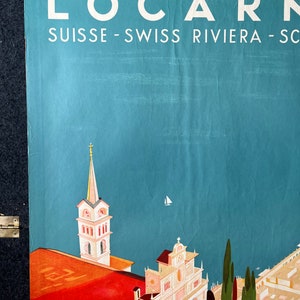 May include: A vintage travel poster advertising the Swiss Riviera town of Locarno. The poster features a colorful illustration of the town's architecture, including a church with a tall spire and a view of the lake. The text on the poster reads "Locarno Suisse - Swiss Riviera - Schweiz - Svizzera - Svizzera Italiana".