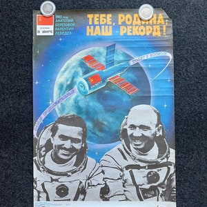 以下が含まれることがあります： ソビエト連邦のヴィンテージなプロパガンダポスター。宇宙服を着た2人の宇宙飛行士が描かれており、「祖国よ、これが私たちの記録だ！」と「宇宙への飛行」というテキストが書かれている。ポスターには、「サリュート7」というテキストと赤い星が描かれた宇宙ステーションが描かれている。