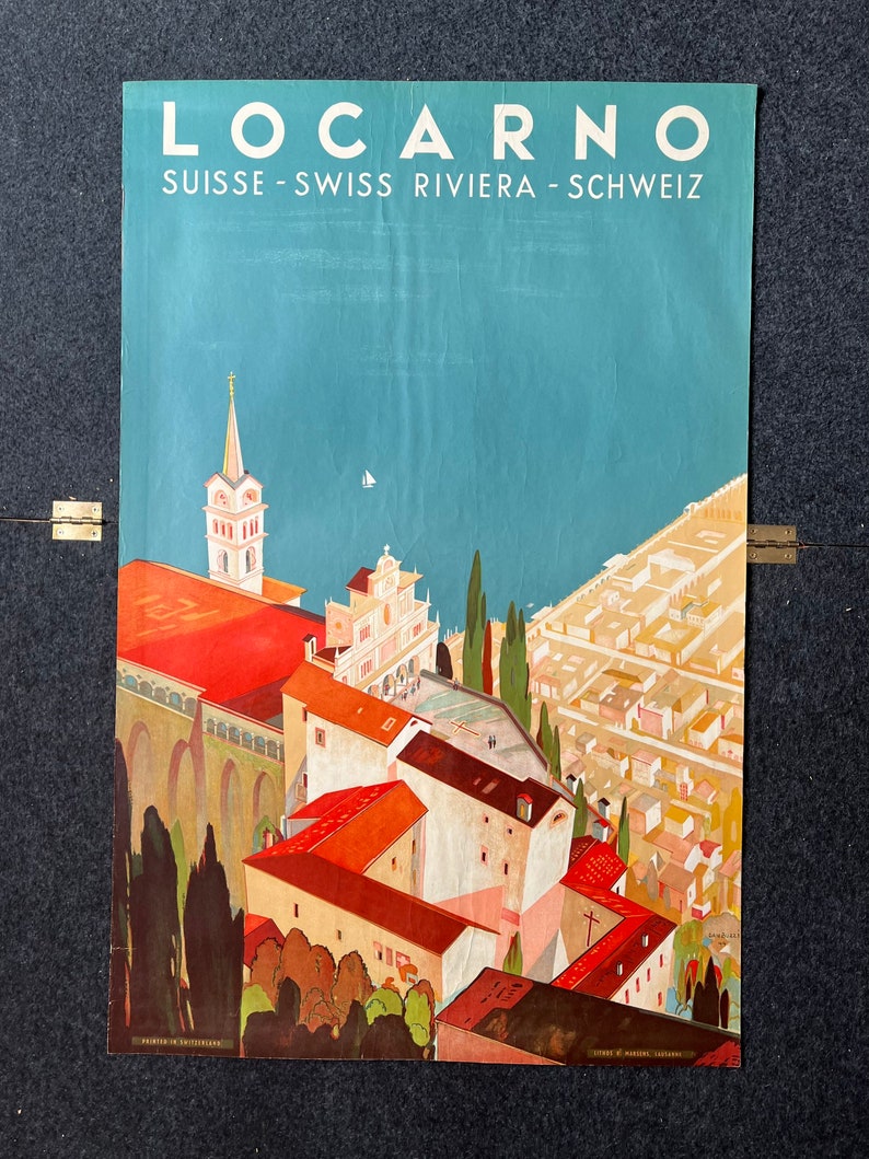 May include: A vintage travel poster advertising the Swiss town of Locarno, featuring a colorful illustration of the town's architecture, including a church with a tall spire, and a view of the lake and surrounding mountains. The poster text reads "Locarno, Suisse - Swiss Riviera - Schweiz".