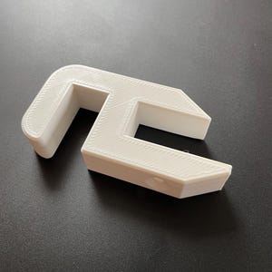 May include: White plastic 3D printed object shaped like a C with a hole in the middle.