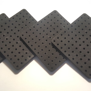May include: Four black square-shaped foam tiles with a grid of small holes. The tiles are arranged in a staggered pattern.