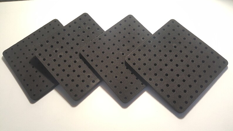 May include: Four black square-shaped foam tiles with a grid of small holes. The tiles are arranged in a staggered pattern.