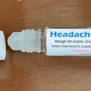 May include: A clear glass roll-on bottle with a white cap, labeled "Headache Relief." The label includes instructions and lists ingredients: Sweet Almond Oil, Lavender, and Peppermint Essential Oils. The bottle is designed for external use.