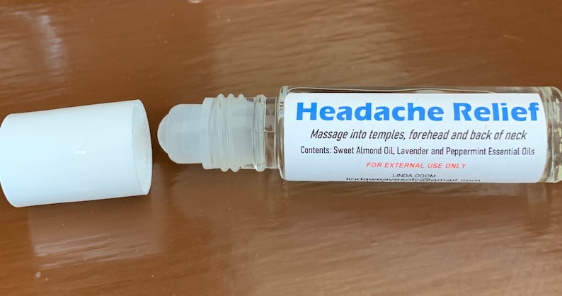 May include: A clear glass roll-on bottle with a white cap, labeled "Headache Relief." The label includes instructions and lists ingredients: Sweet Almond Oil, Lavender, and Peppermint Essential Oils. The bottle is designed for external use.