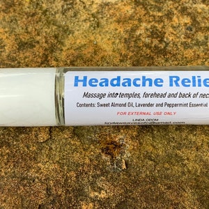 May include: A clear glass roll-on bottle with a white cap and a label that reads "Headache Relief." The label includes instructions and ingredients: Sweet Almond Oil, Lavender, and Peppermint Essential Oils. For external use only.