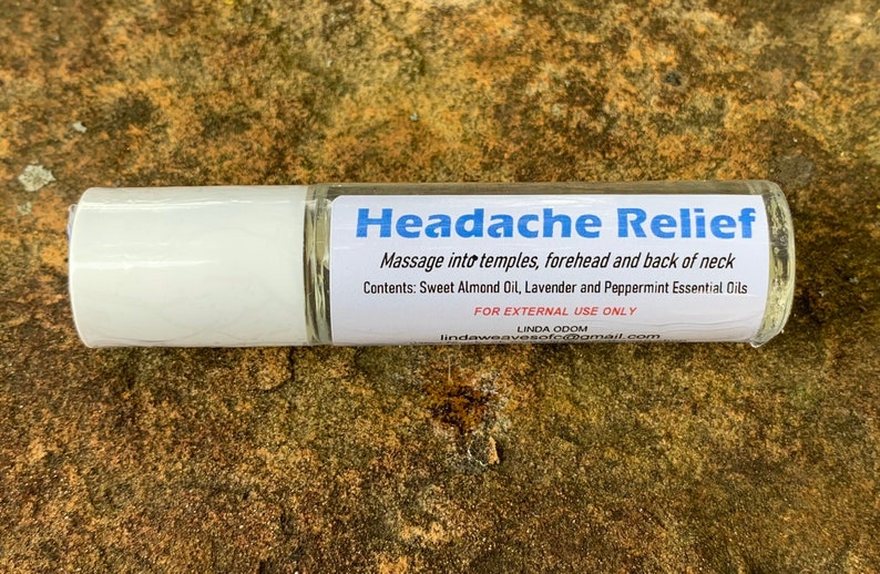 May include: A clear glass roll-on bottle with a white cap and a label that reads "Headache Relief." The label includes instructions and ingredients: Sweet Almond Oil, Lavender, and Peppermint Essential Oils. For external use only.