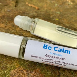 May include: A white roller bottle with a label that reads "Be Calm" and "For relaxation Apply to pulse points Contents: Sweet Almond Oil, Lavender, Orange, Cedarwood & Frankincense Essential Oils FOR EXTERNAL USE ONLY".