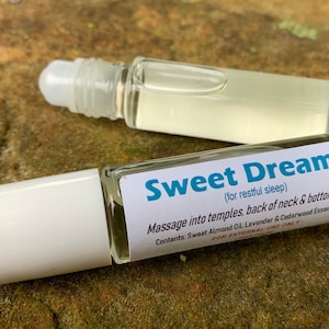May include: A white roller bottle with a blue label that reads "Sweet Dreams (for restful sleep)". The label also includes instructions for use and a list of ingredients: Sweet Almond Oil, Lavender & Cedarwood Essential Oils.  FOR EXTERNAL USE ONLY.