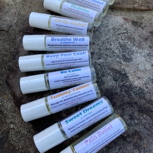 May include: A collection of roll-on essential oil blends with white caps and labels. The labels feature text such as "Stay Focused!", "Headache Relief", and "De-Stress". The bottles are arranged on a textured, natural surface.